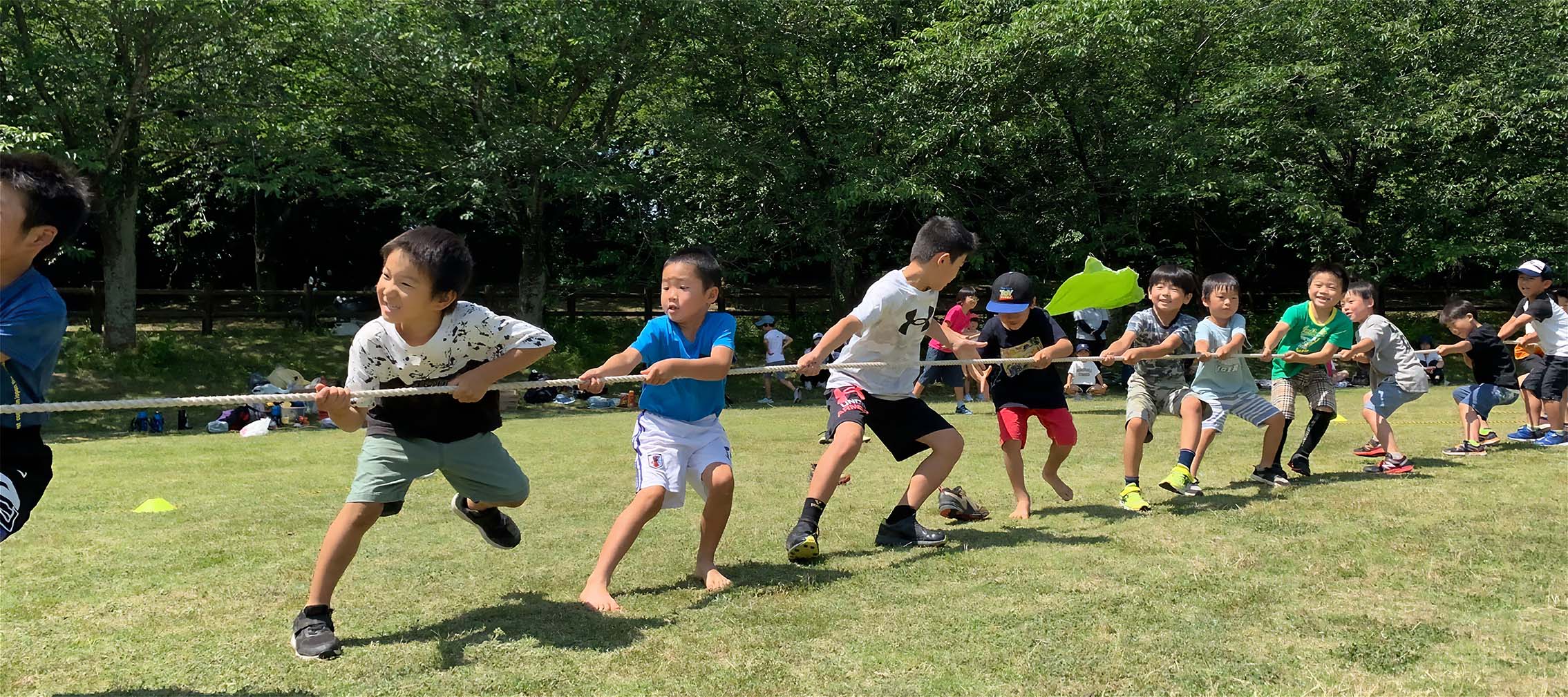 青空の下綱引きをする学童の子どもたちの様子